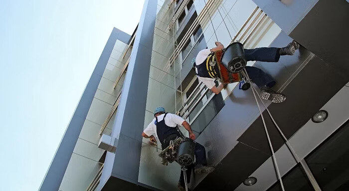 Two workers suspended on ropes cleaning the exterior windows of a modern building