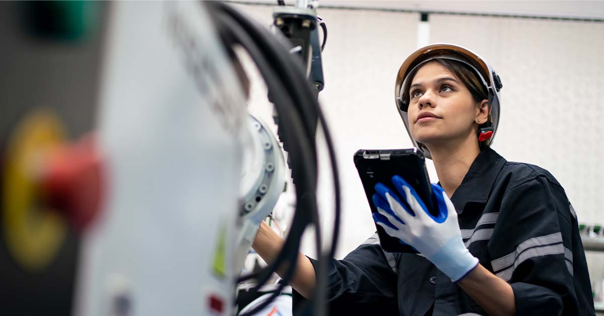 Female engineer inspecting industrial machinery using a tablet.