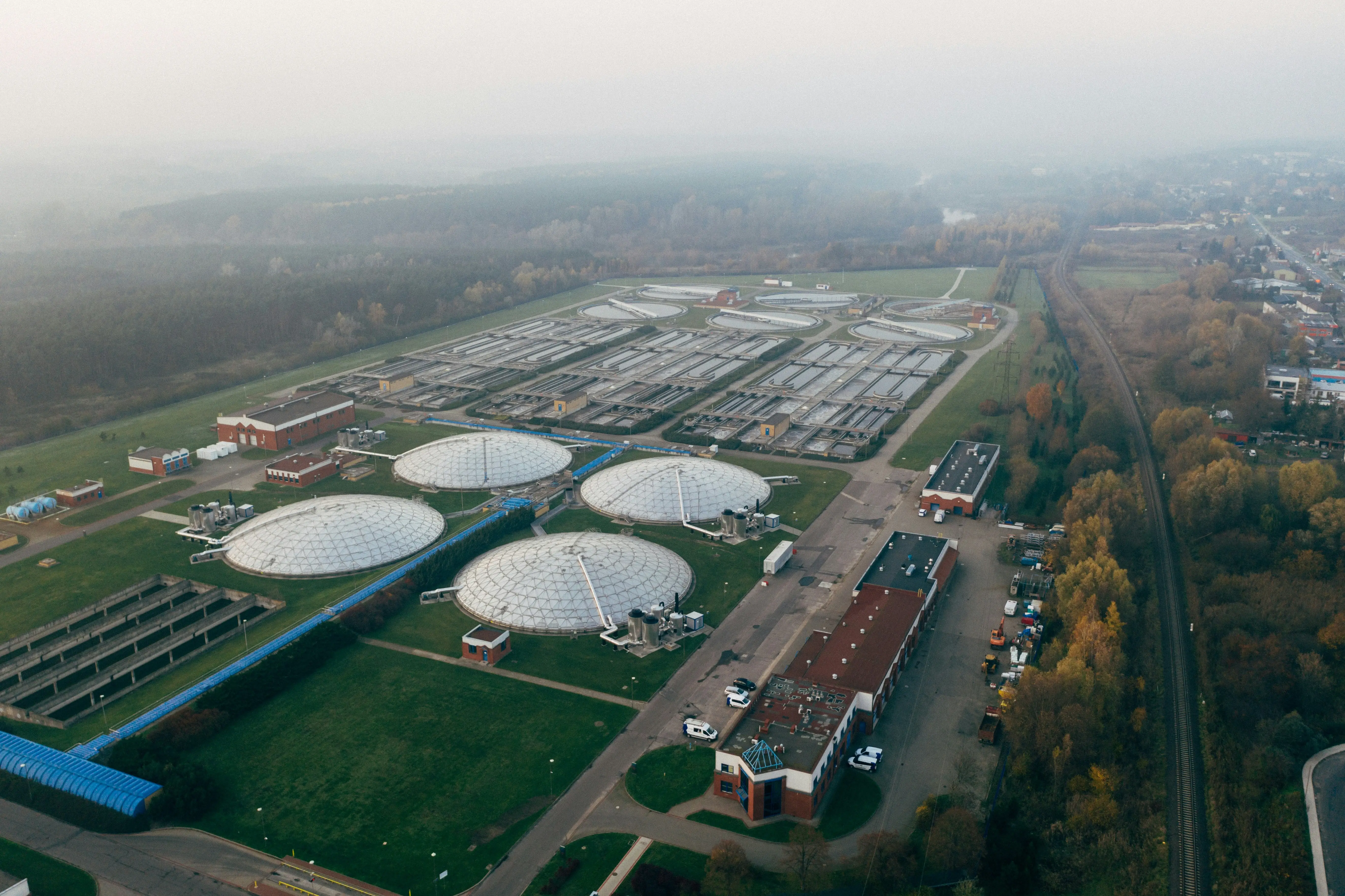 An aerial view of a large wastewater treatment facility with multiple circular tanks and rectangular basins surrounded by greenery