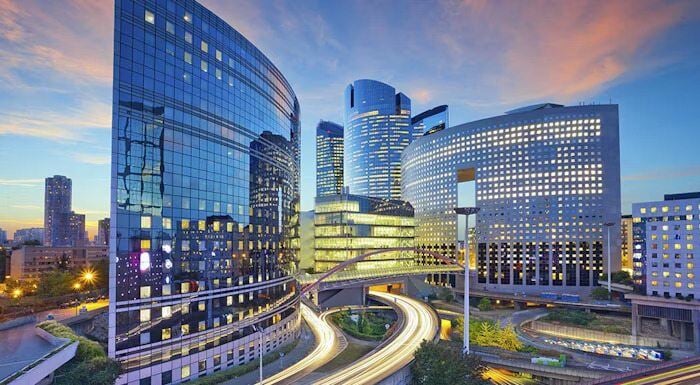 A modern cityscape with glass skyscrapers and light trails from traffic at dusk