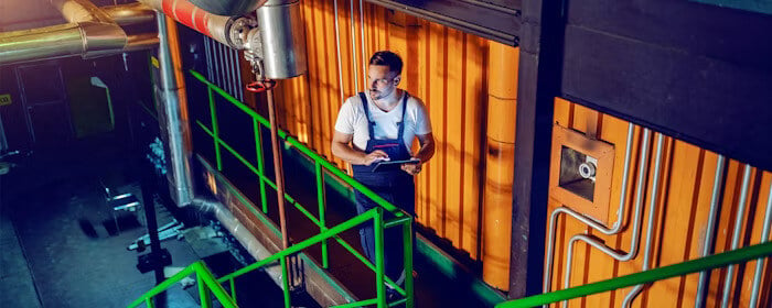 A worker using a tablet while inspecting equipment in an industrial facility