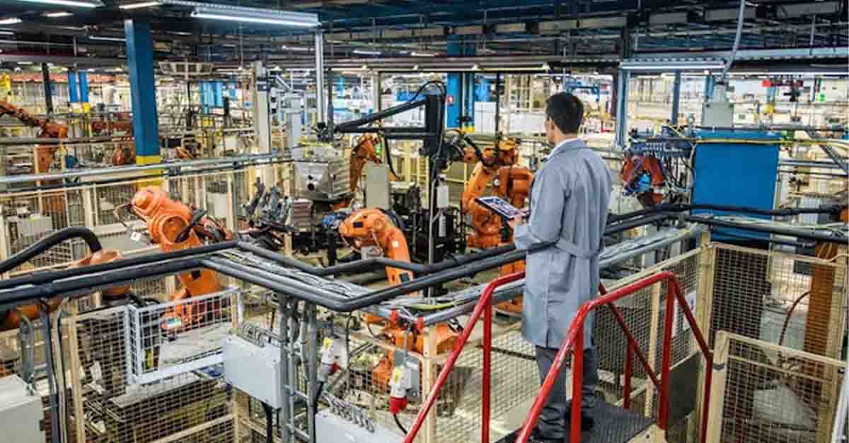 An engineer overlooking a factory floor filled with robotic arms and industrial machinery