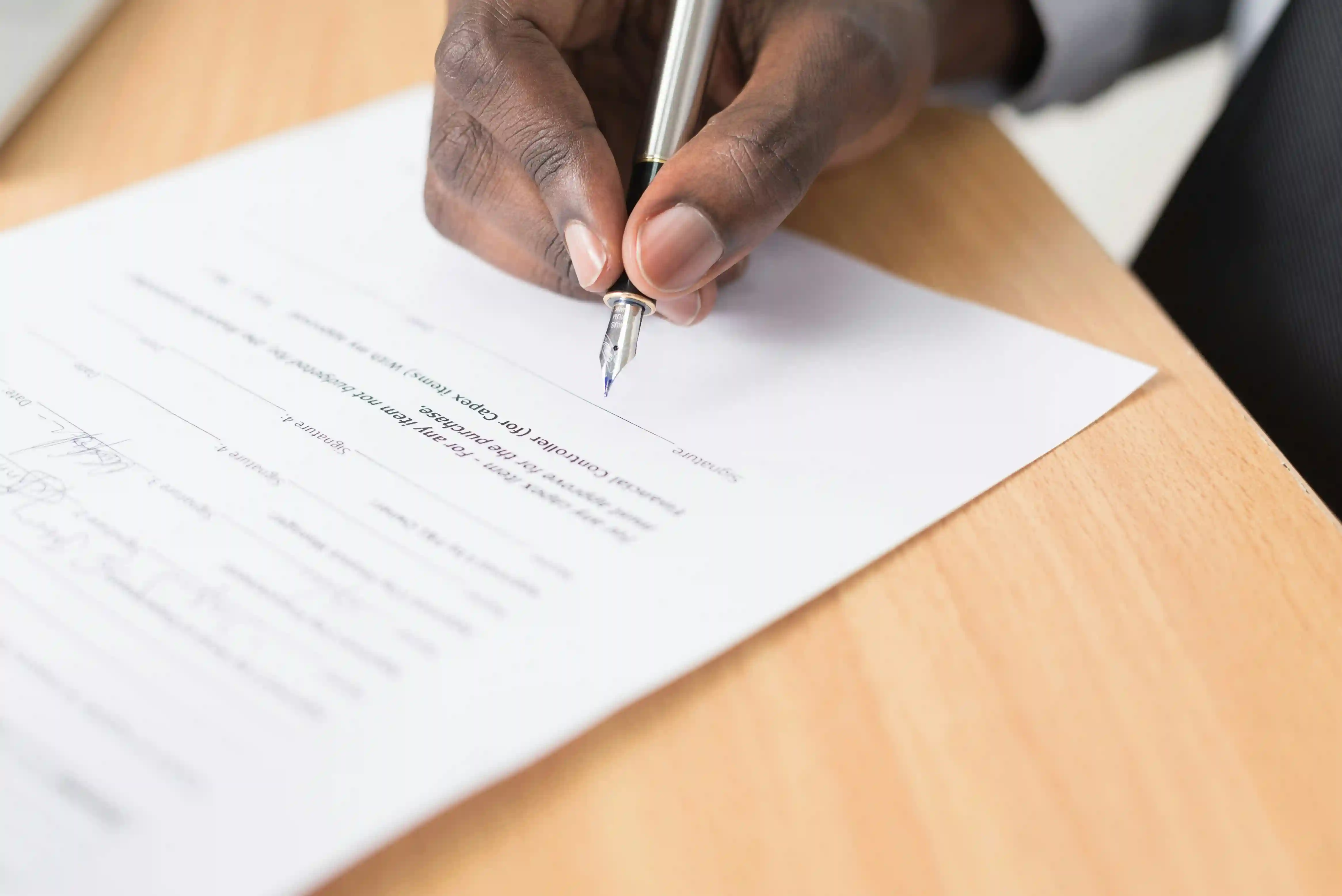 Close-up of a person signing a document with a fountain pen on a wooden desk