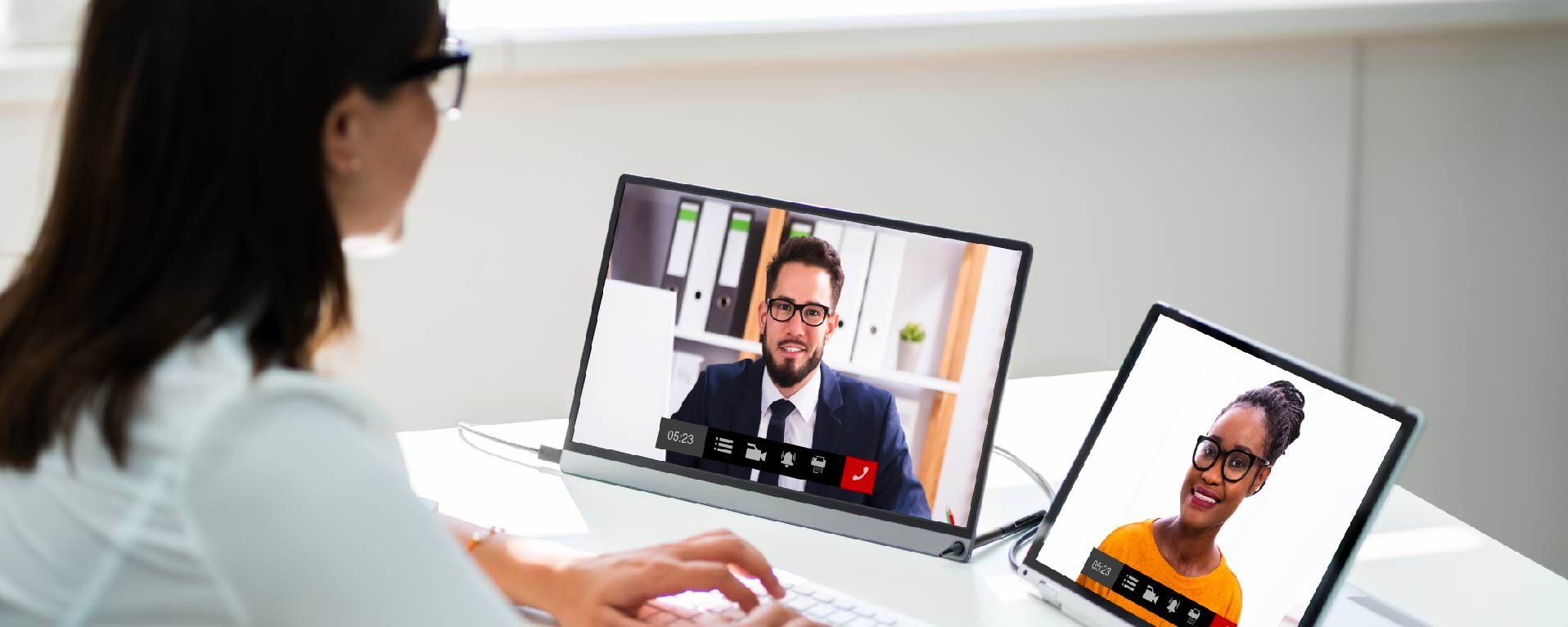 A person participates in a video conference, viewing two colleagues on separate screens during a virtual meeting