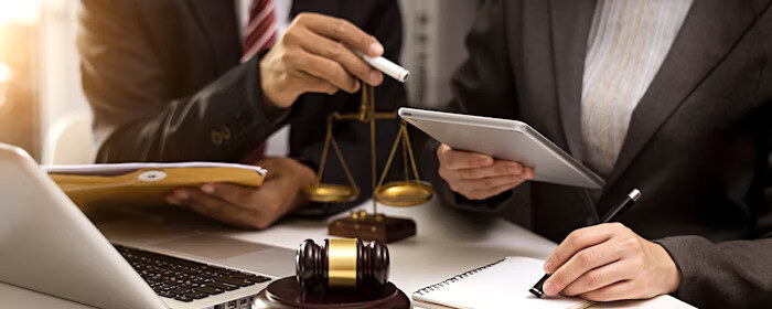 Two professionals review documents and use a tablet at a desk with legal symbols, including a gavel and scales of justice