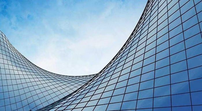 Curved glass facade of a modern building reflecting the blue sky