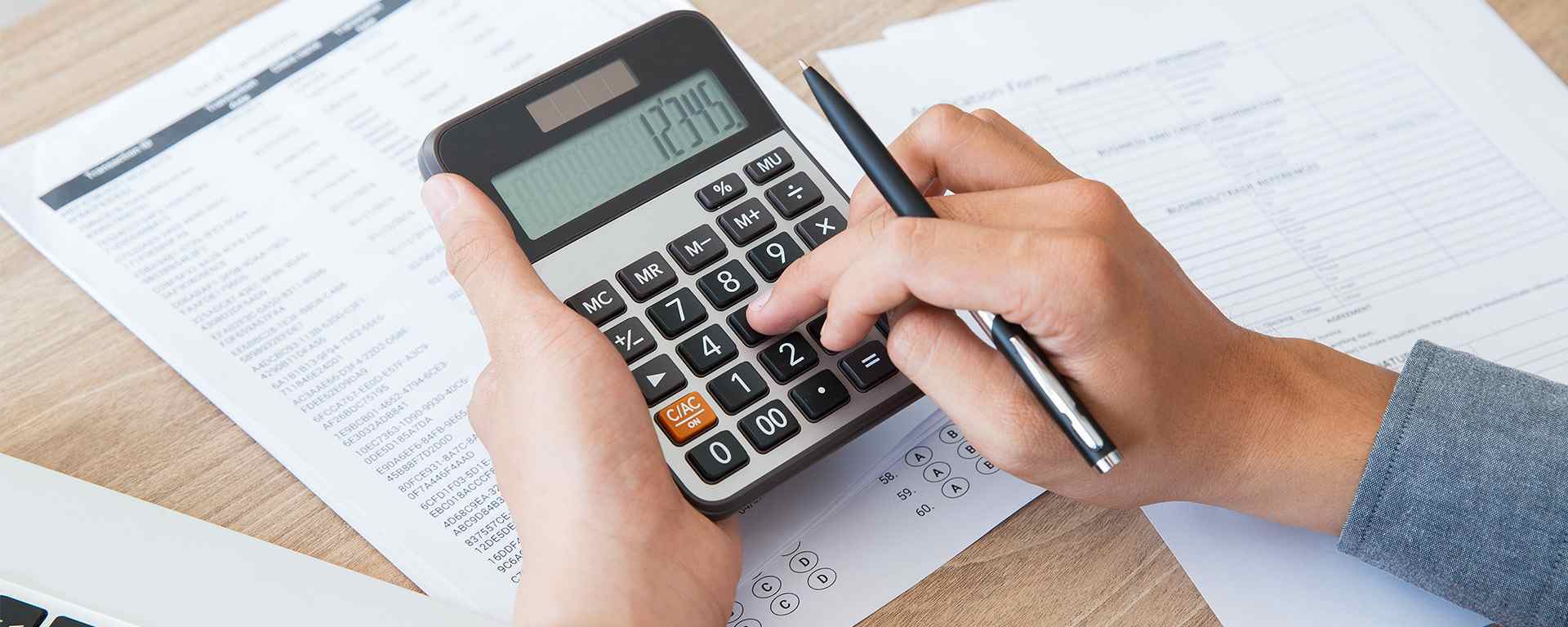 Close-up of a person using a calculator and pen to work on financial documents