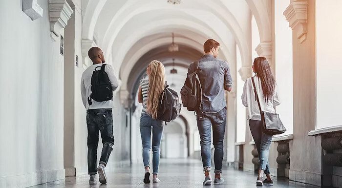 A group of students with backpacks walk down a bright, arched hallway