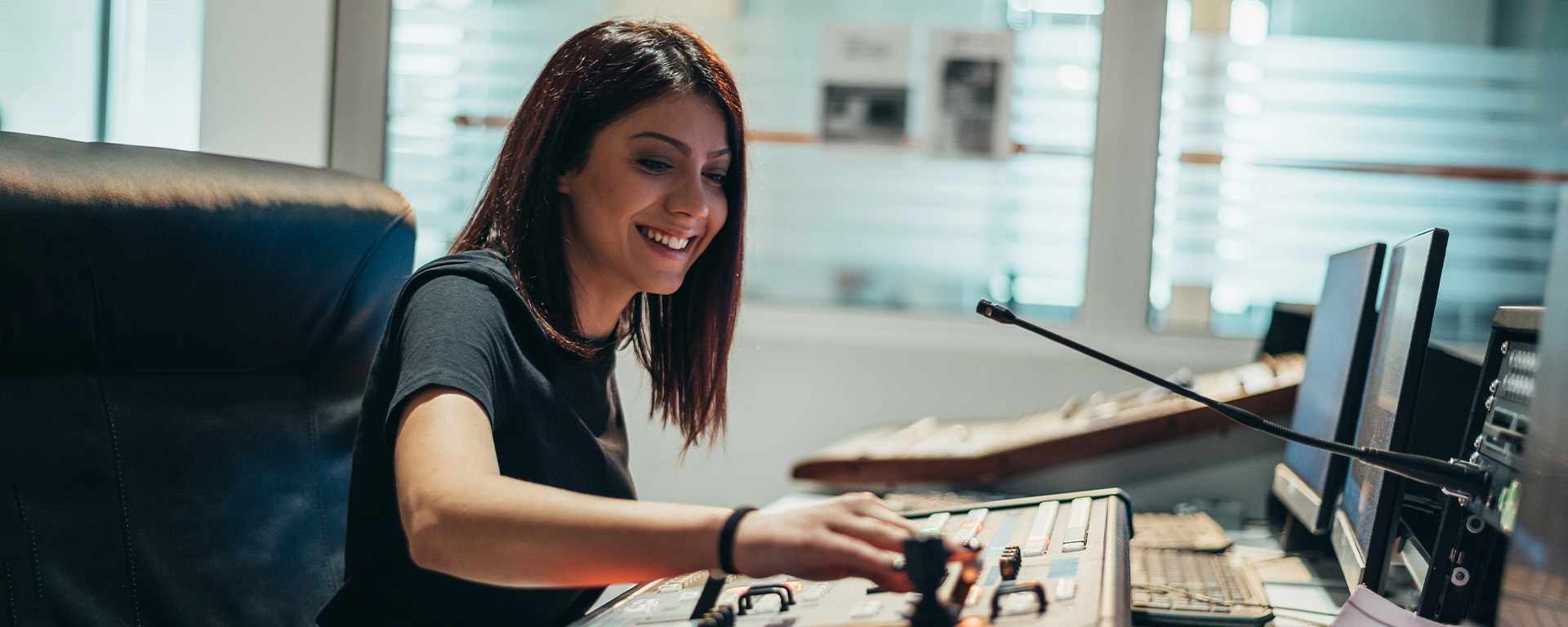 A smiling woman operating a control panel in a modern broadcast center