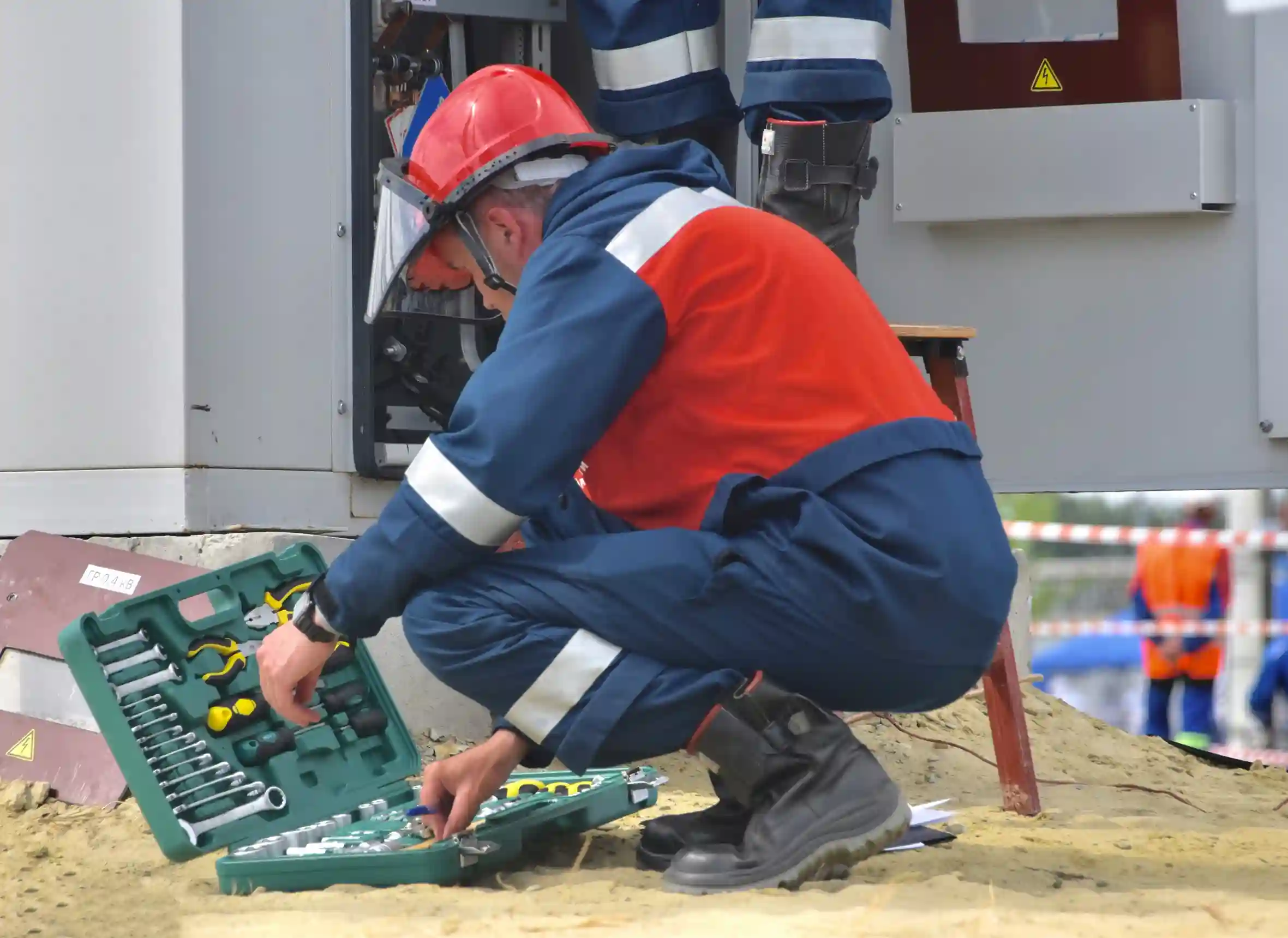 Technician in safety gear working on electrical equipment with a tool kit