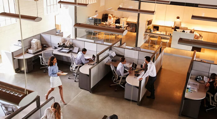 An open office space with employees working at their desks in cubicles, while others walk around or engage in conversations