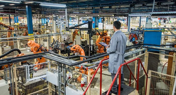 An engineer overlooking a factory floor filled with robotic arms and industrial machinery