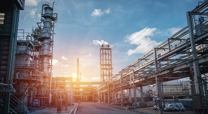 An industrial refinery with pipelines and towers under a blue sky during sunset