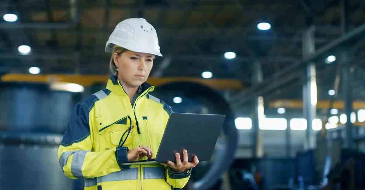 Female engineer in a hard hat and high-visibility jacket using a laptop in an industrial facility