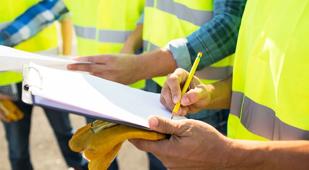 Construction workers in reflective vests writing notes on a clipboard during a site inspection