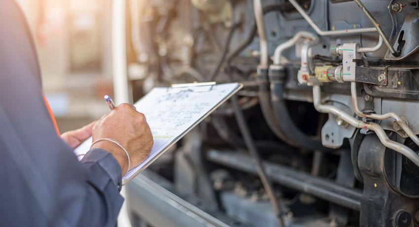 A technician inspecting a machine and writing notes on a clipboard