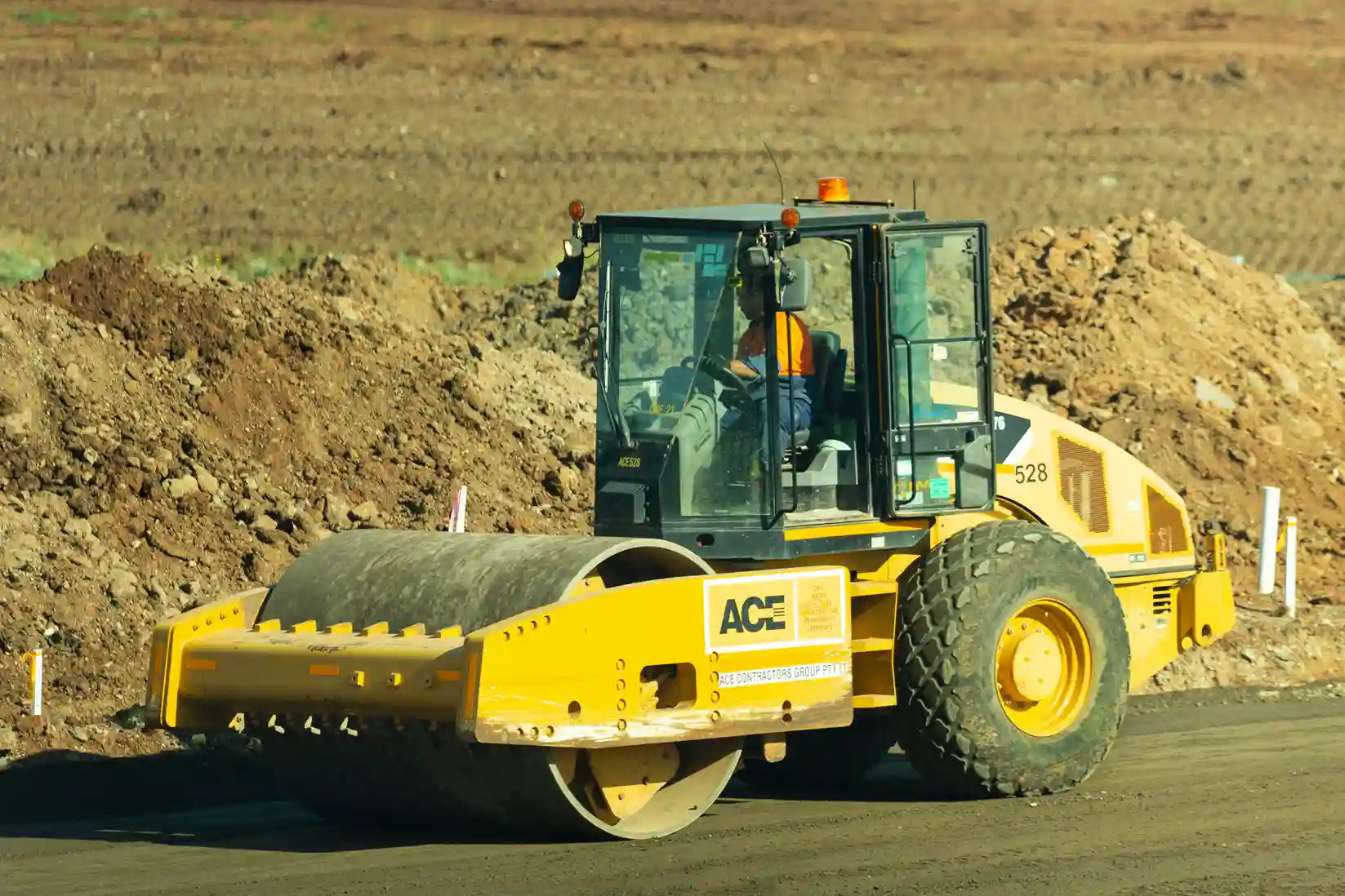 Construction worker operating a yellow road roller on a dirt site