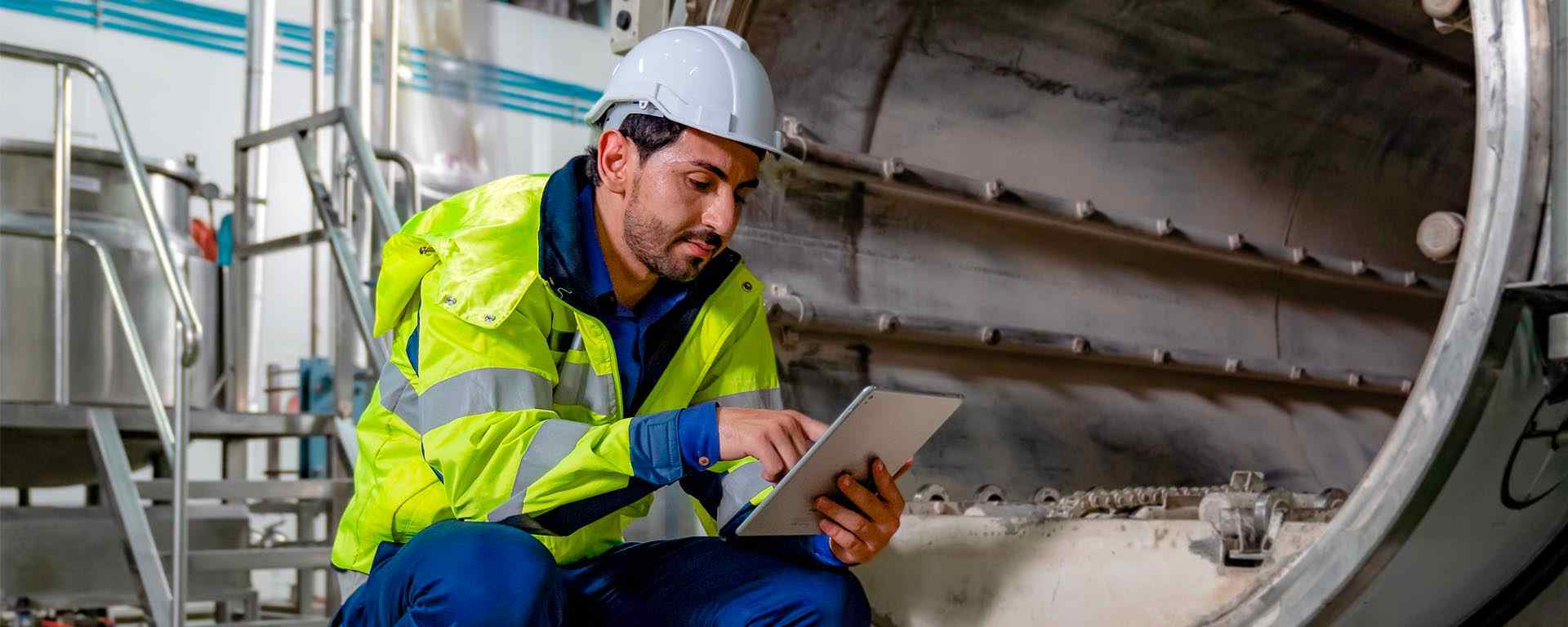 Engineer wearing a reflective jacket and safety helmet using a tablet in an industrial setting