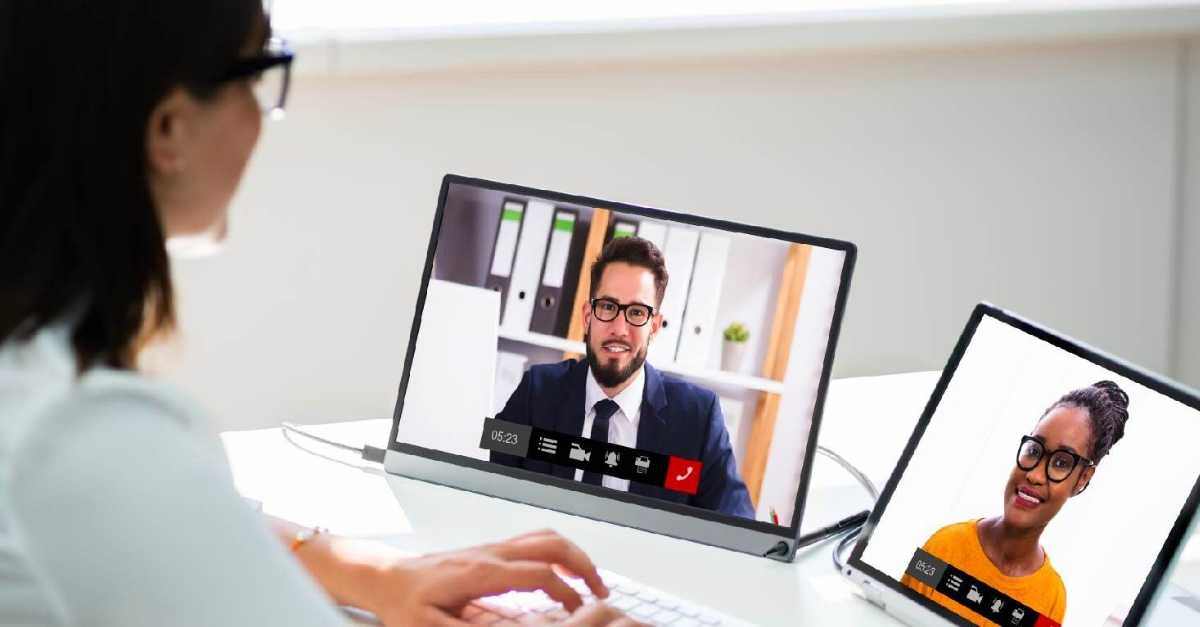 A person participates in a video conference, viewing two colleagues on separate screens during a virtual meeting