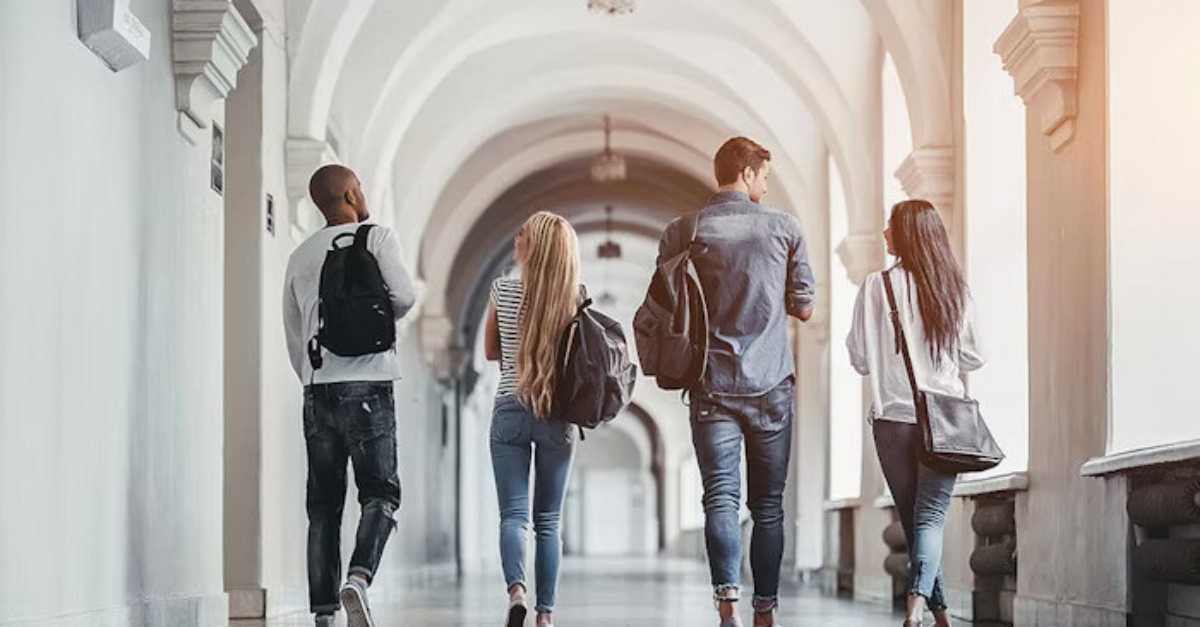 A group of students with backpacks walk down a bright, arched hallway