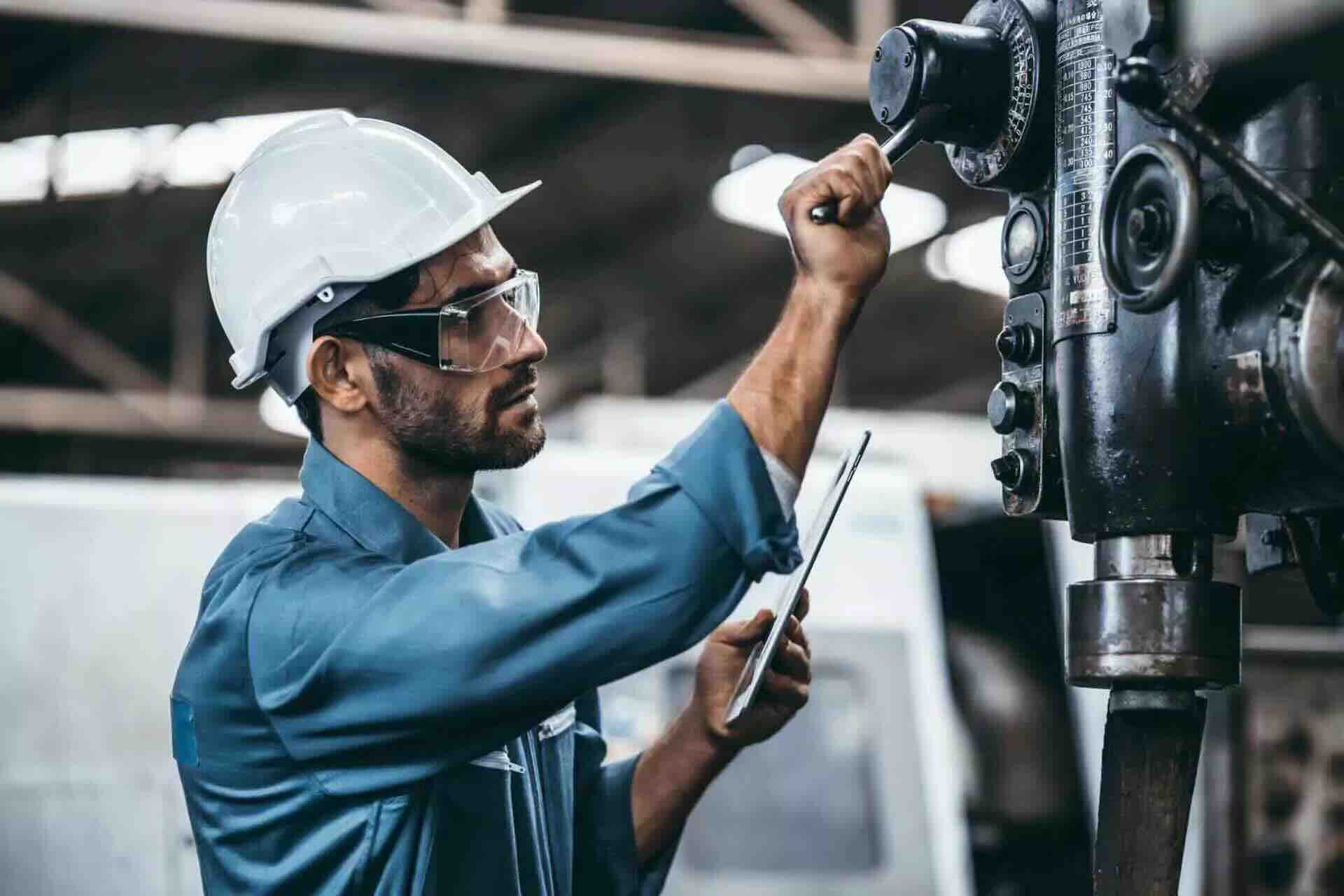 Engineer in a hard hat using a tablet while adjusting machinery