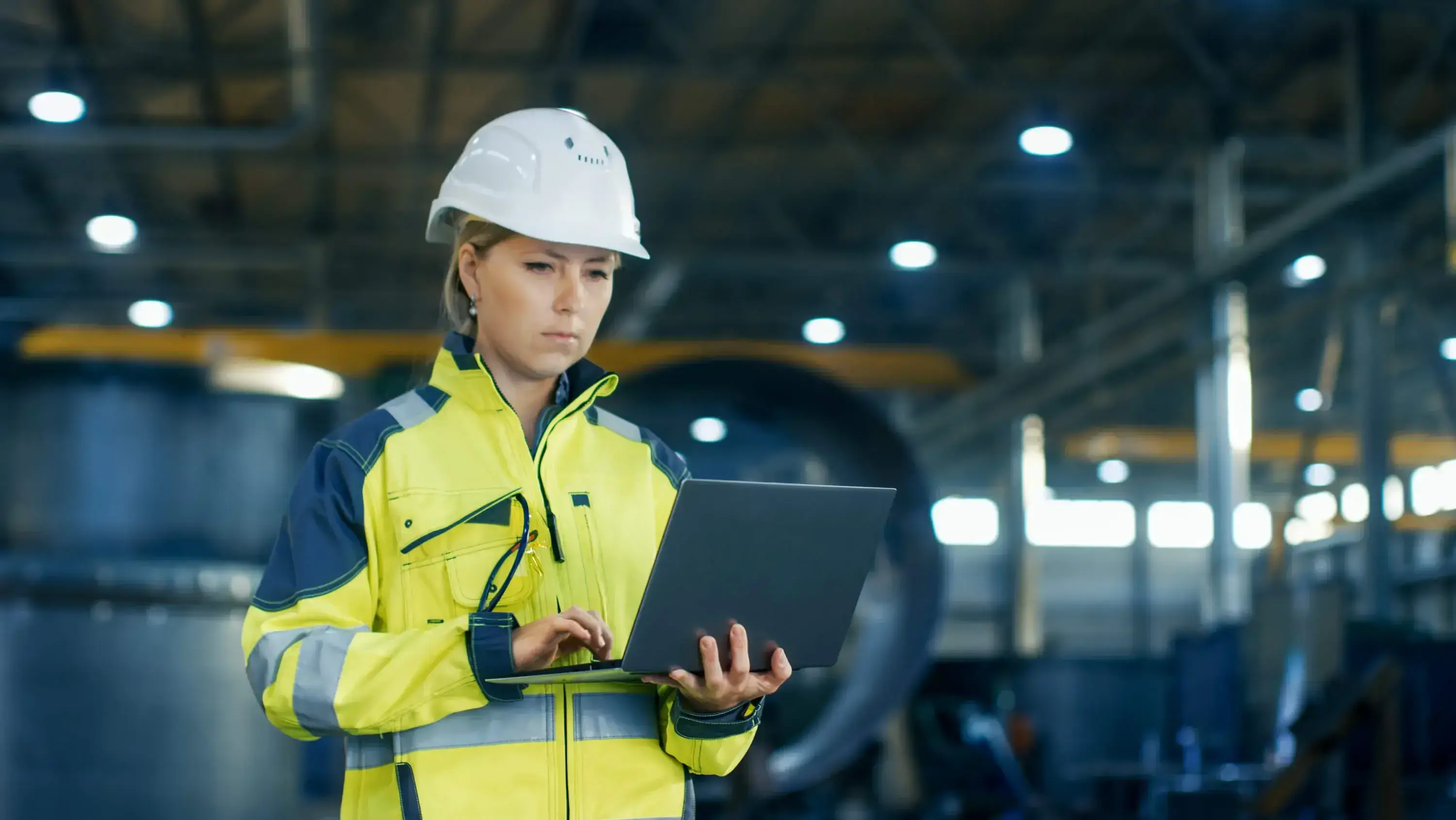 Female engineer in a hard hat and high-visibility jacket using a laptop in an industrial facility