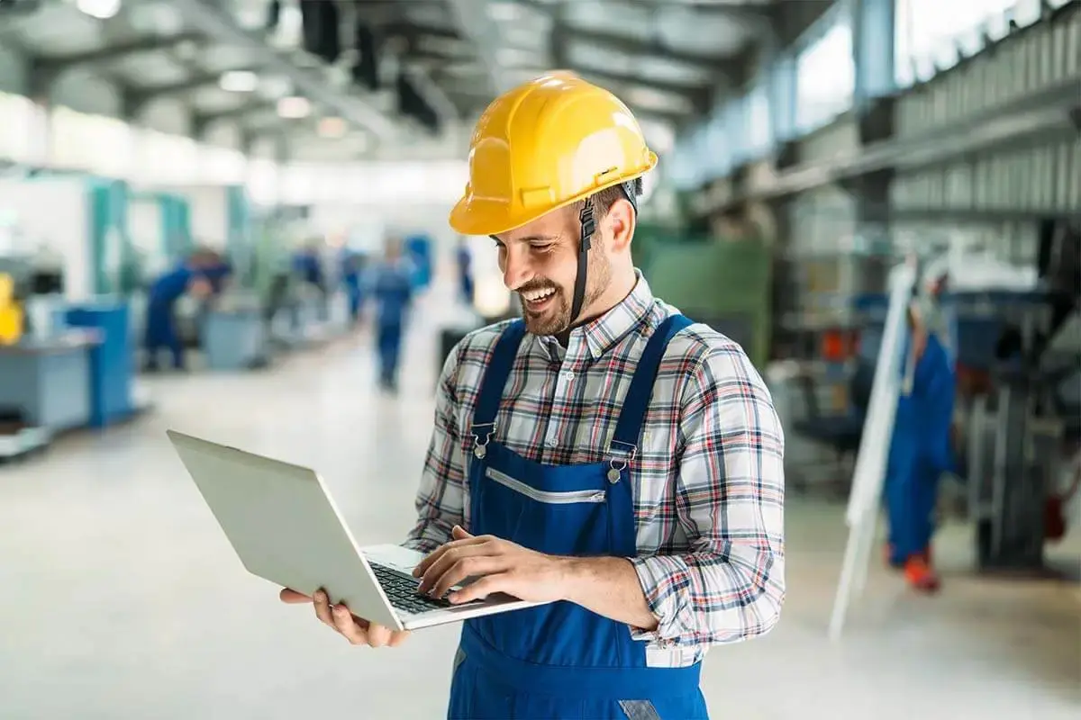 A factory employee efficiently manages maintenance tasks using CMMS software on a computer, ensuring smooth operations.