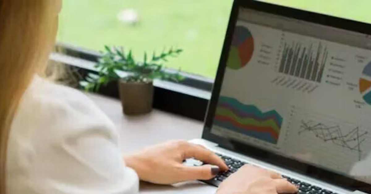 A person works on a laptop displaying various colorful data charts and graphs